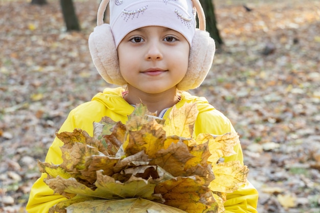 Klein schattig meisje met boeket gele gevallen bladeren in de herfst in het park