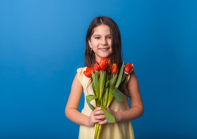 Klein schattig meisje met een boeket tulpen op een blauwe achtergrond Gelukkige vrouwendag Plaats voor tekst Levendige emoties 8 maart