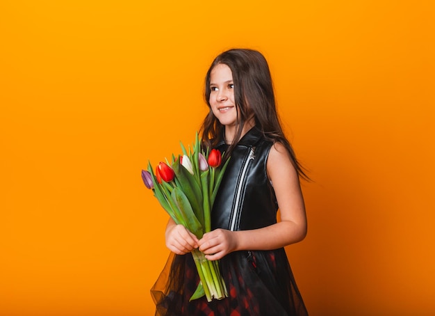 Klein schattig meisje met een boeket tulpen op een gele achtergrond gelukkige vrouwendag plaats voor tekst levendige emoties 8 maart