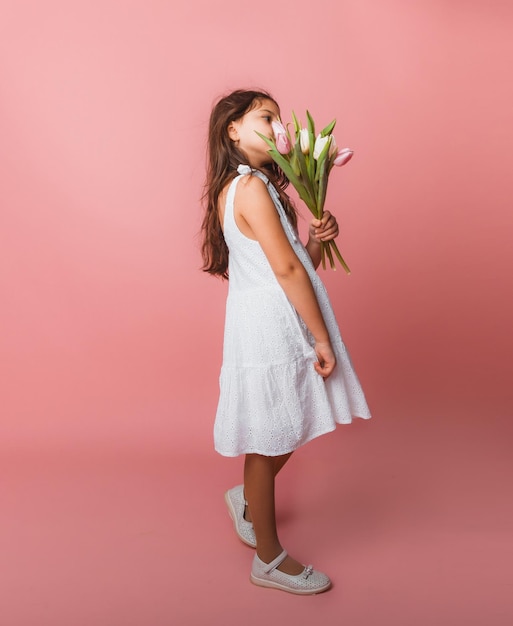 Klein schattig meisje met een boeket tulpen op een roze achtergrond Gelukkige vrouwendag Plaats voor tekst Levendige emoties 8 maart