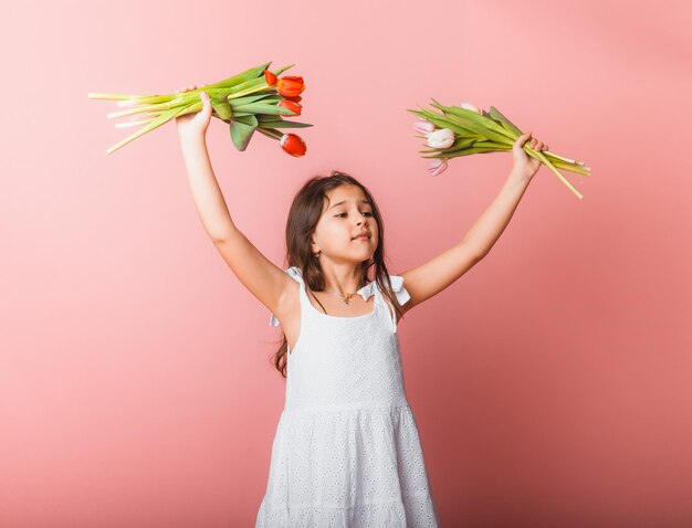 Klein schattig meisje met een boeket tulpen op een roze achtergrond Gelukkige vrouwendag Plaats voor tekst Levendige emoties 8 maart