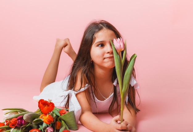 Klein schattig meisje met een boeket tulpen op een roze achtergrond Gelukkige vrouwendag Plaats voor tekst Levendige emoties 8 maart