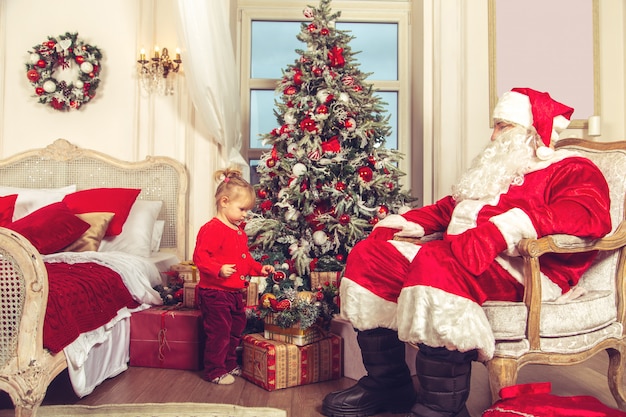 Klein schattig meisje met een echte kerstman in de buurt van de kerstboom.