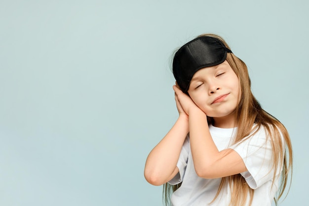 Klein schattig meisje met een slaapmasker wil slapen op een blauwe achtergrond Problemen met slapeloosheid bij kinderen