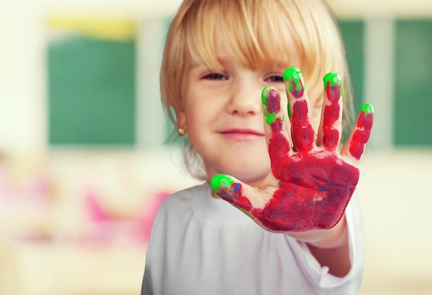 Klein schattig meisje met hand in gekleurde verf