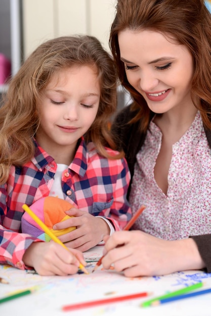 Klein schattig meisje met moeder tekenen aan tafel thuis