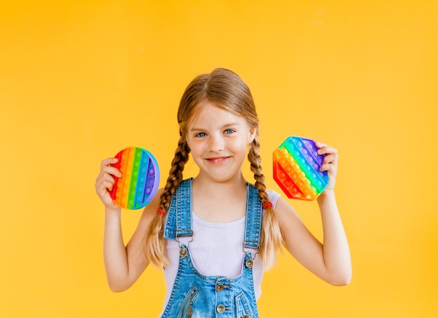 Klein schattig meisje met pop-it anti-stress speelgoed op gele achtergrond, isoleren. kopieerruimte