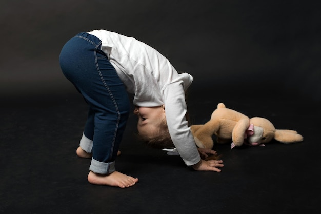 Klein schattig meisje ondersteboven lopen op haar armen in studio op zwarte achtergrond