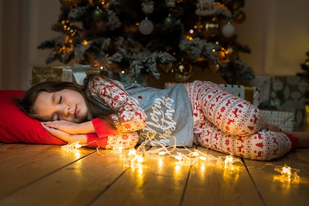 Foto klein schattig meisje slaapt in de buurt van een kerstboom en wacht op santa happy child dreaming gifts