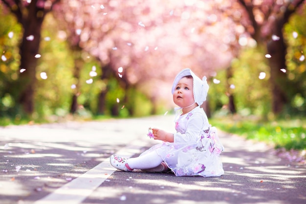 Klein schattig meisje speelt onder bloeiende kersenboom met roze bloemen in een prachtige lentetuin