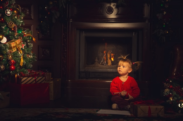 Klein schattig meisje spelen in de woonkamer in de buurt van de kerstboom.