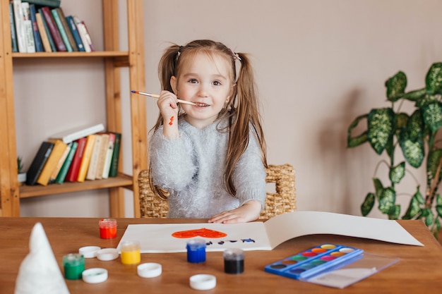 Klein schattig meisje tekent met verf aan de tafel in de woonkamer