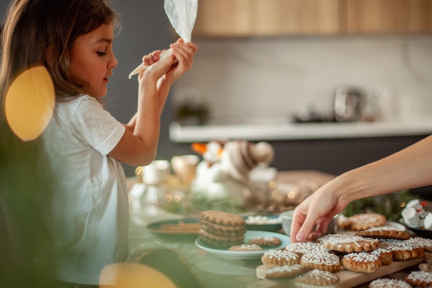 Klein schattig meisje versiert peperkoek met suikerglazuur voorbereiding voor kerstconcept