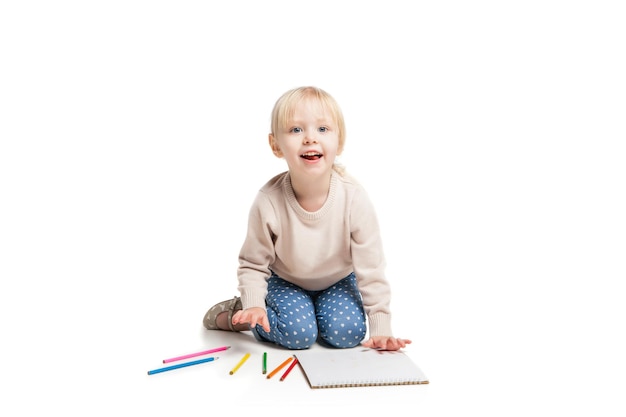 Klein schattig meisje zittend op de vloer en tekenen met kleurrijke potloden geïsoleerd op wit