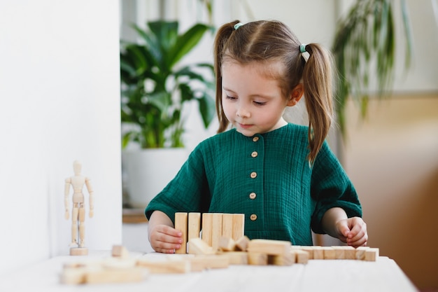 Klein schattig voorschoolse meisje speelt thuis met houten speelgoed op tafel. Natuurlijke tactiliteit ontwikkeling.