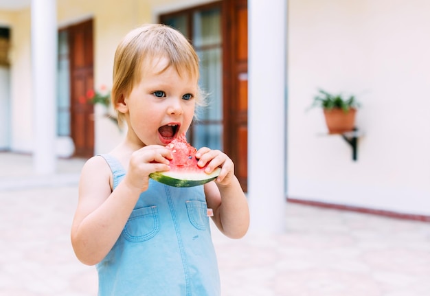 Klein schattig vrolijk meisje dat een plakje watermeloen van dichtbij eet