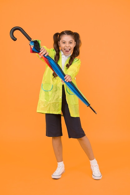 Klein schoolmeisje draagt waterbestendige kleding voor een regenachtige dag. Leuk schoolmeisje voelt zich beschermd voor lenteweer. Waterdicht concept. Match je regenjas met paraplu. Schoolmeisje draagt regenjas.