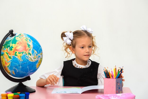 klein schoolmeisje zit aan de tafel te studeren op een afgelegen witte achtergrond S