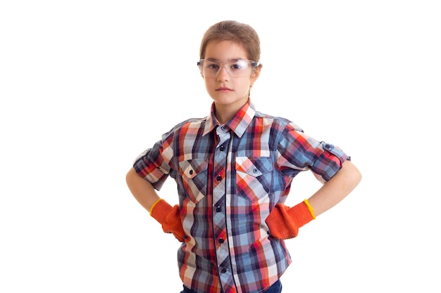 Klein serieus meisje met lange kastanjebruine staart in geruit rood shirt met oranje handschoenen en bril