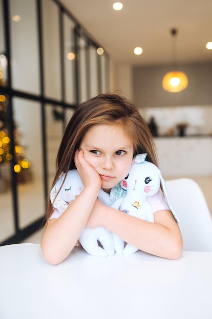 Klein verdrietig meisje knuffelt favoriete speeltje terwijl ze aan tafel zit