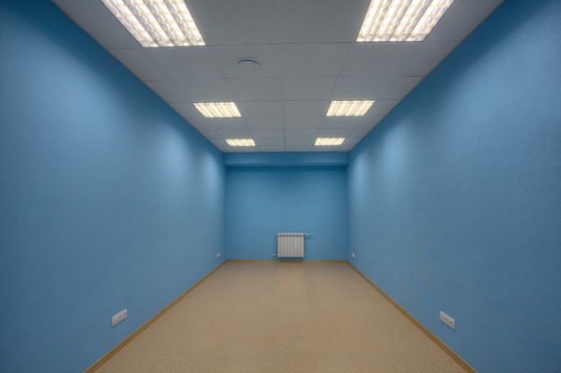 Klein verlaten ongemeubileerd kantoor, geen lichaam en geen ramen, de muren zijn blauw geverfd.
