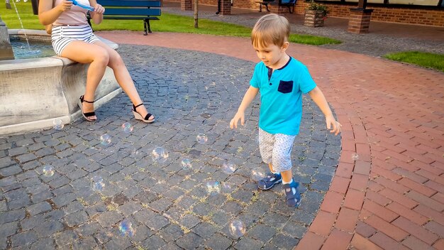 Kleine 3 jaar oude peuter die achter kleurrijke zeepbellen aan rent op het stadsplein