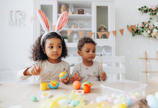 Kleine Afro-Amerikaanse jongen en meisje schilderen thuis paaseieren, zwarte kinderen bereiden zich voor op Pasen