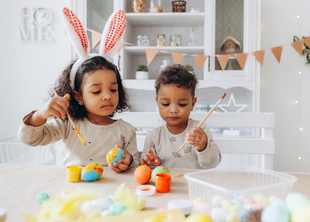 Kleine Afro-Amerikaanse jongen en meisje schilderen thuis paaseieren, zwarte kinderen bereiden zich voor op Pasen