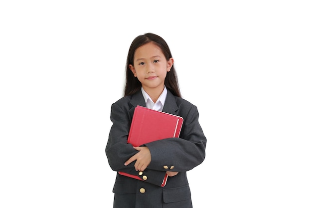 Kleine aziatische schoolmeisje in formele slijtage shirt, pak knuffelen een boek tijdens het kijken naar camera geïsoleerd op witte achtergrond.