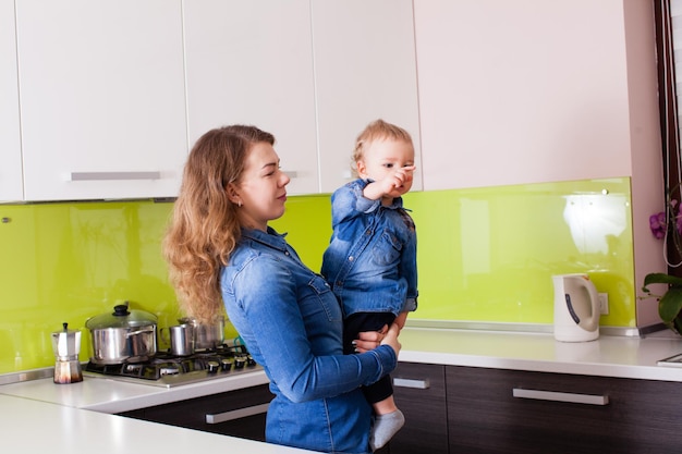 Kleine baby in de armen van moeder in hun keuken. De jongen wijst op iets met zijn wijsvinger