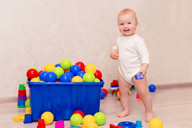 Kleine baby in witte kleren zit en speelt met ballen