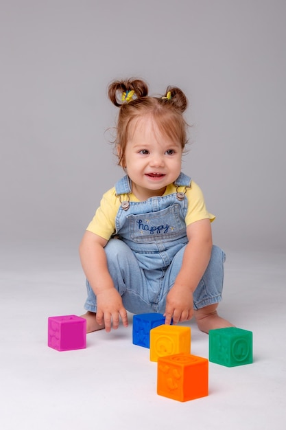 kleine baby meisje zit op witte achtergrond spelen met kleurrijke kubussen kid's play speelgoed kubussen