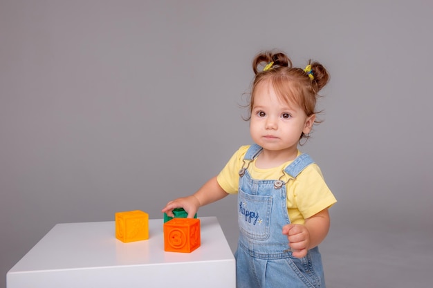 kleine baby meisje zit op witte achtergrond spelen met kleurrijke kubussen kid's play speelgoed kubussen