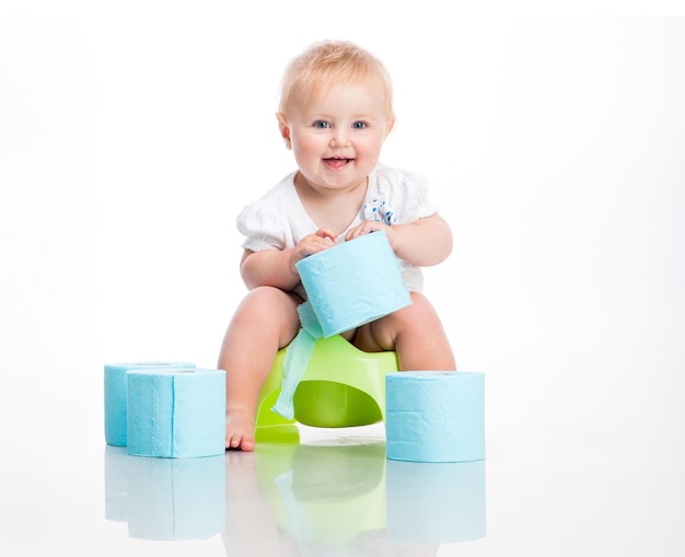 kleine baby zit op een pot en houdt de toiletpapier studio foto op witte achtergrond