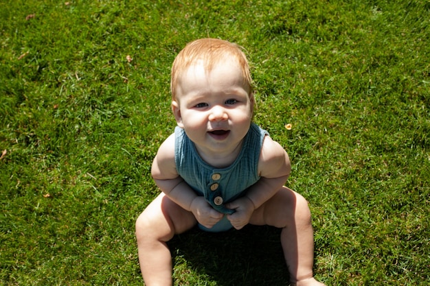 Kleine baby zit op het gras in het park en glimlachtZomer en felle zonBuitenwandeling
