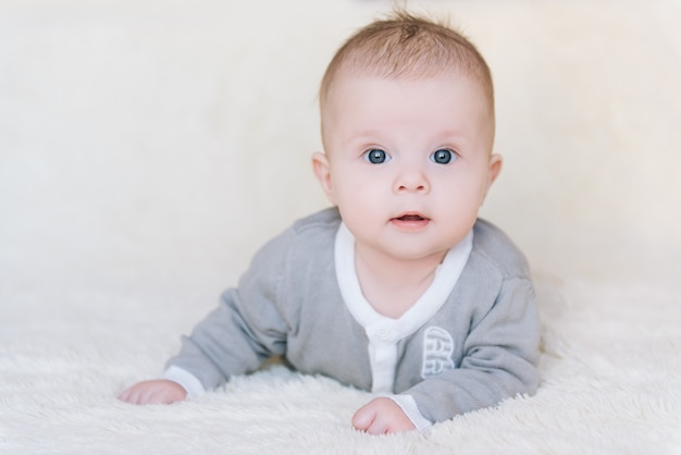 Kleine babyjongen die op maag ligt en zijn hoofd opheft terwijl verrast en leuk, pasgeboren glimlachen kijkt