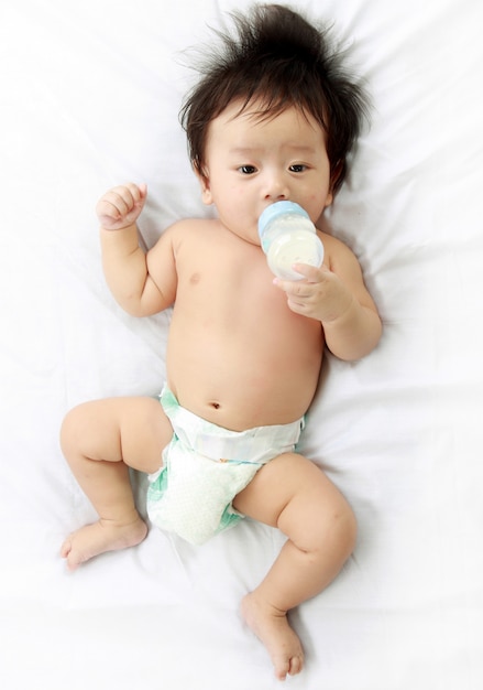 kleine babyjongen drinkt melk uit de fles door hemzelf vastgehouden, liggend op bed