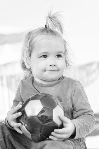 Foto kleine babyjongen of schattig kind met blij gezicht en blond haar in groen shirt en broek zitten spelen met kleurrijke bal op zonnige zomer buiten strand op natuurlijke hemelachtergrond