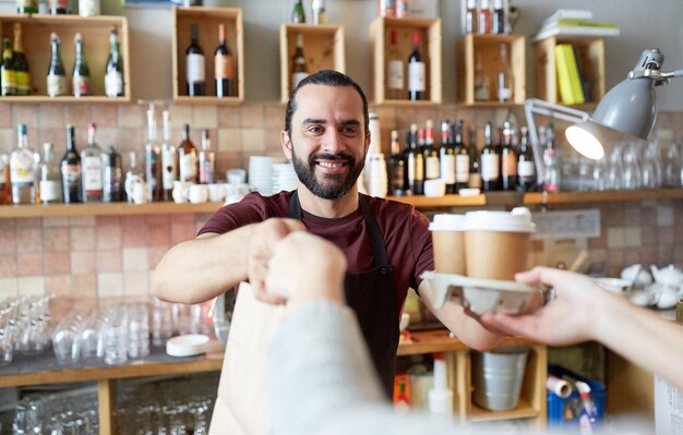 Foto kleine bedrijven, mensen, takeaway en service concept - gelukkige man of ober die zakjes en papieren bekers met warme dranken geeft aan klanten in een koffieshop