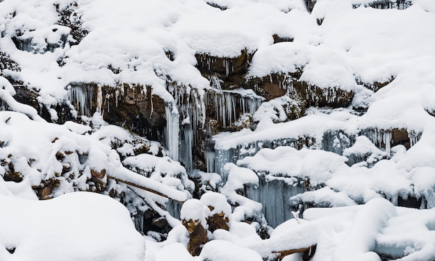 Kleine bergwaterval van ijskoude waterstroom tussen natte stenen bedekt met witte sneeuw