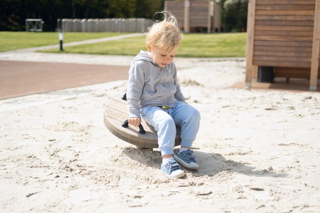 Kleine blanke blonde jongen spelen op kinderspeelplaats in een zonnige herfstdag.