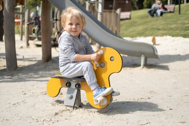 Kleine blanke blonde jongen spelen op kinderspeelplaats in een zonnige herfstdag.