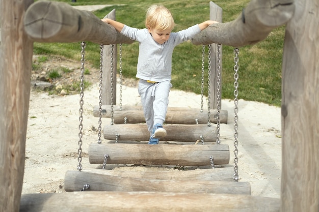 Kleine blanke blonde jongen spelen op kinderspeelplaats in een zonnige herfstdag.