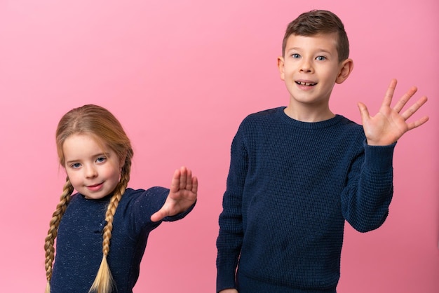 Kleine blanke broers geïsoleerd op roze achtergrond die met de hand groeten met een gelukkige uitdrukking