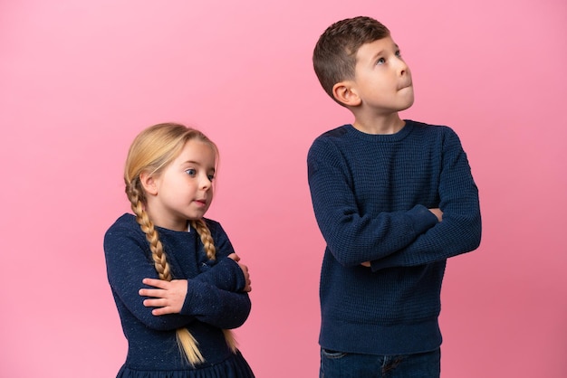 Kleine blanke broers geïsoleerd op roze achtergrond die twijfels gebaar maken terwijl ze de schouders optillen