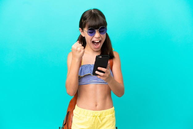 Kleine blanke jongen gaat naar het strand geïsoleerd op blauwe achtergrond met telefoon in overwinningspositie