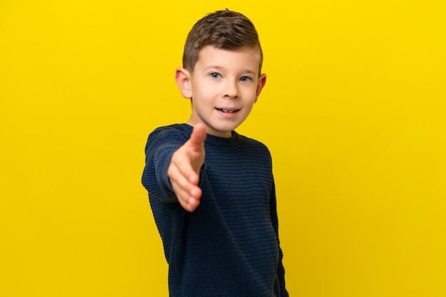 Kleine blanke jongen geïsoleerd op gele achtergrond handen schudden voor het sluiten van een goede deal