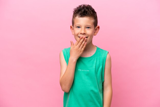 Kleine blanke jongen geïsoleerd op roze achtergrond gelukkig en glimlachend die mond bedekken met hand