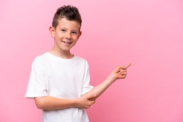 Kleine blanke jongen geïsoleerd op roze achtergrond wijzende vinger naar de zijkant