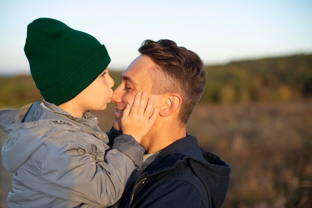 Foto kleine blanke jongen kust zijn gelukkig lachende vader buitenshuis close-up portret